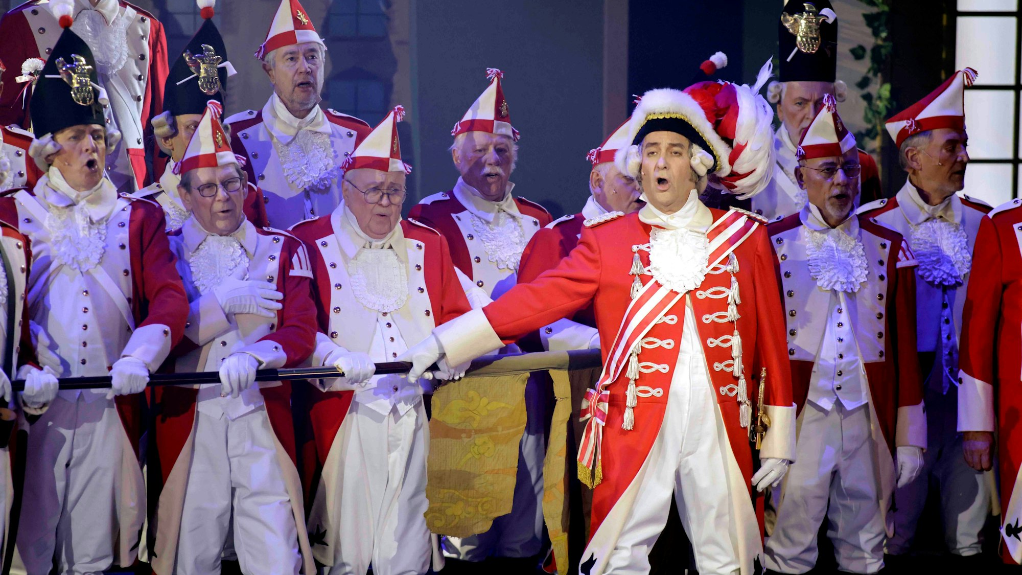 Einige Männer stehen in Karnevalsuniformen auf der Bühne.