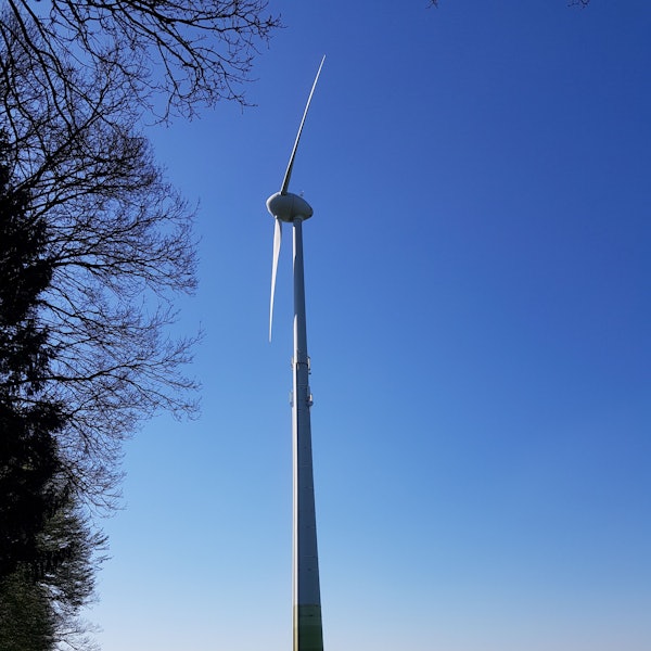 Die Flügel einer Windkraftanlage sind vor blauem Himmel zu sehen.