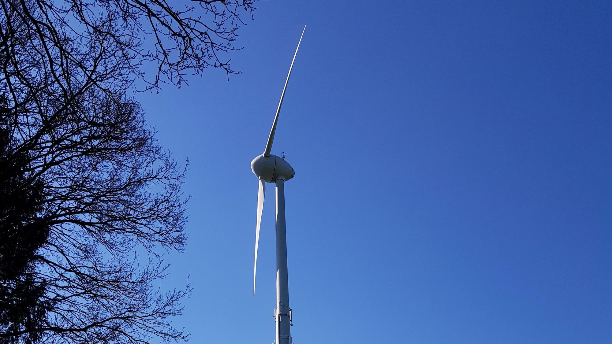 Die Flügel einer Windkraftanlage sind vor blauem Himmel zu sehen.