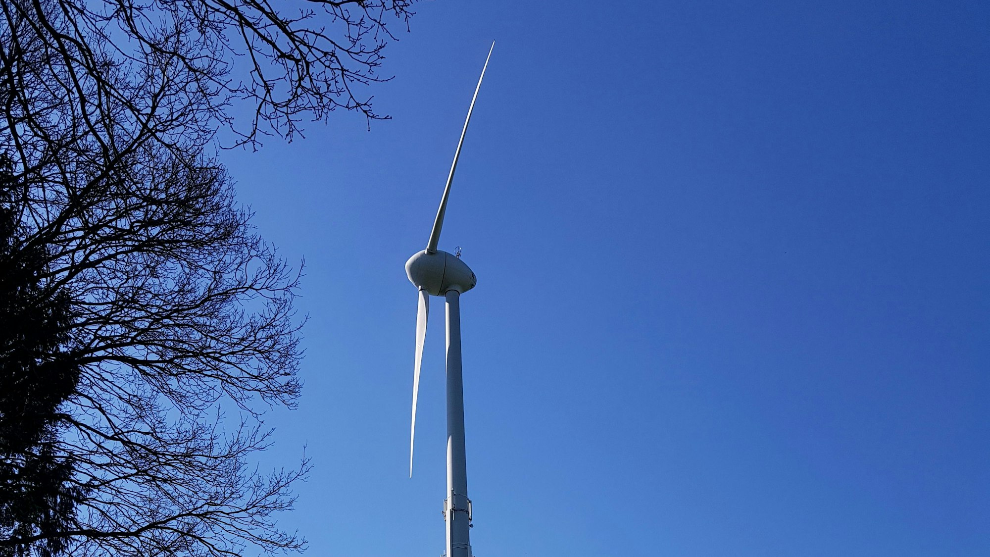 Die Flügel einer Windkraftanlage sind vor blauem Himmel zu sehen.