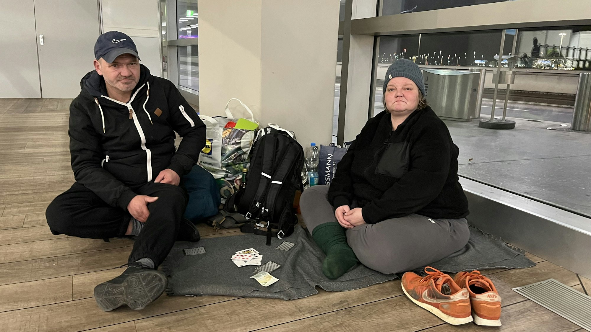 Die Obdachlose Margarete Zehnpfennig und ihr Freund Mariusz sitzen auf Decken im Terminal 1 des Flughafens und spielen Karten.