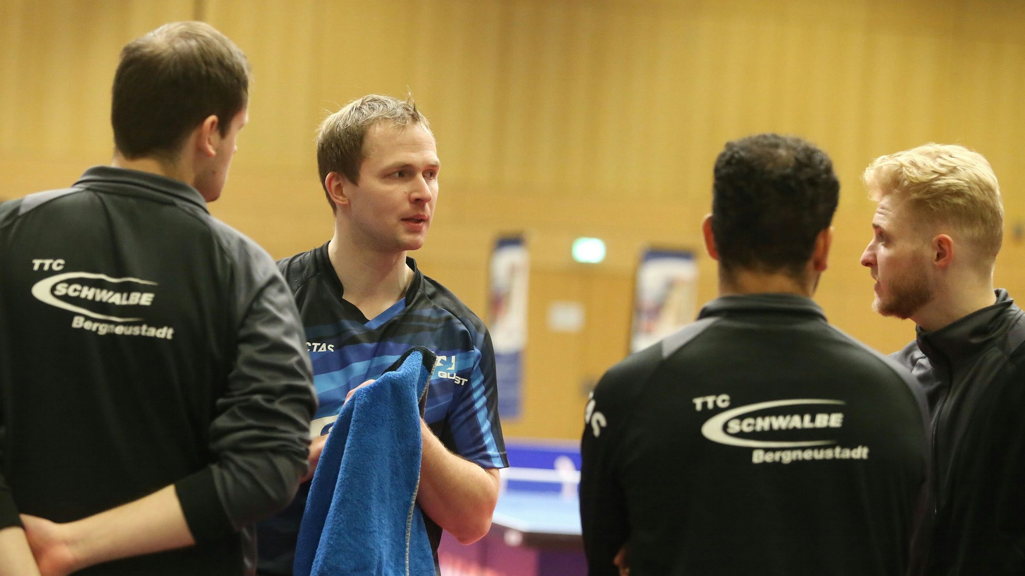 Mehrere Mannschaftskollegen einer Tischtennismannschaft stehen in einem Kreis und beraten sich. Einer hält ein blaues Handtuch in der Hand.