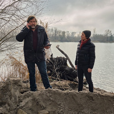 Die Kommissare Franziska Tobler (Eva Löbau) und Friedemann Berg (Hans-Jochen Wagner) stehen am Ufer eines Sees. Vor ihnen ist Erde aufgeschüttet.
