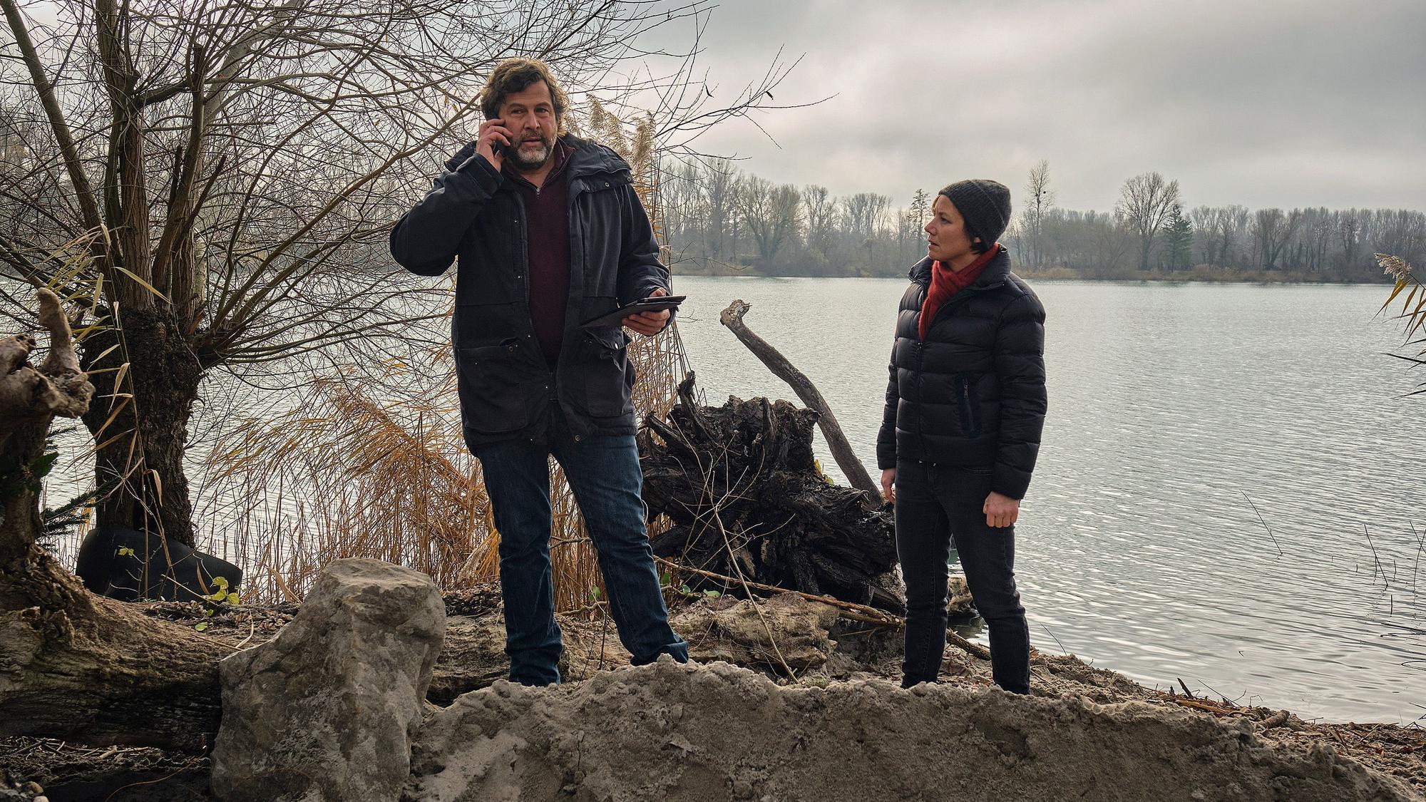 Die Kommissare Franziska Tobler (Eva Löbau) und Friedemann Berg (Hans-Jochen Wagner) stehen am Ufer eines Sees. Vor ihnen ist Erde aufgeschüttet.