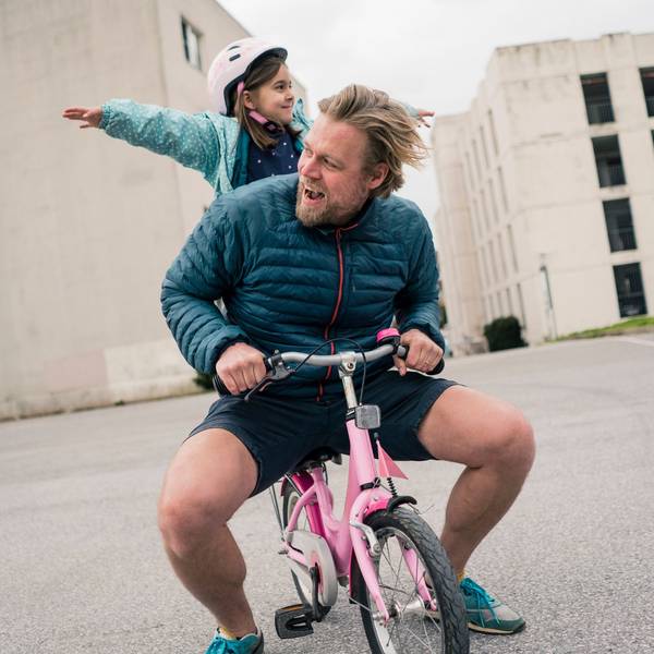 Junger Vater sitzt mit seinem Kind auf einem pinkfarbenen Dreirad (Symbolbild)