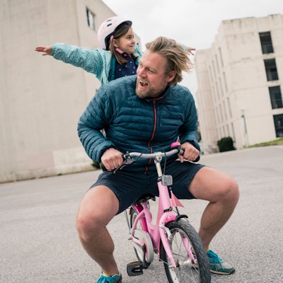 Junger Vater sitzt mit seinem Kind auf einem pinkfarbenen Dreirad (Symbolbild)