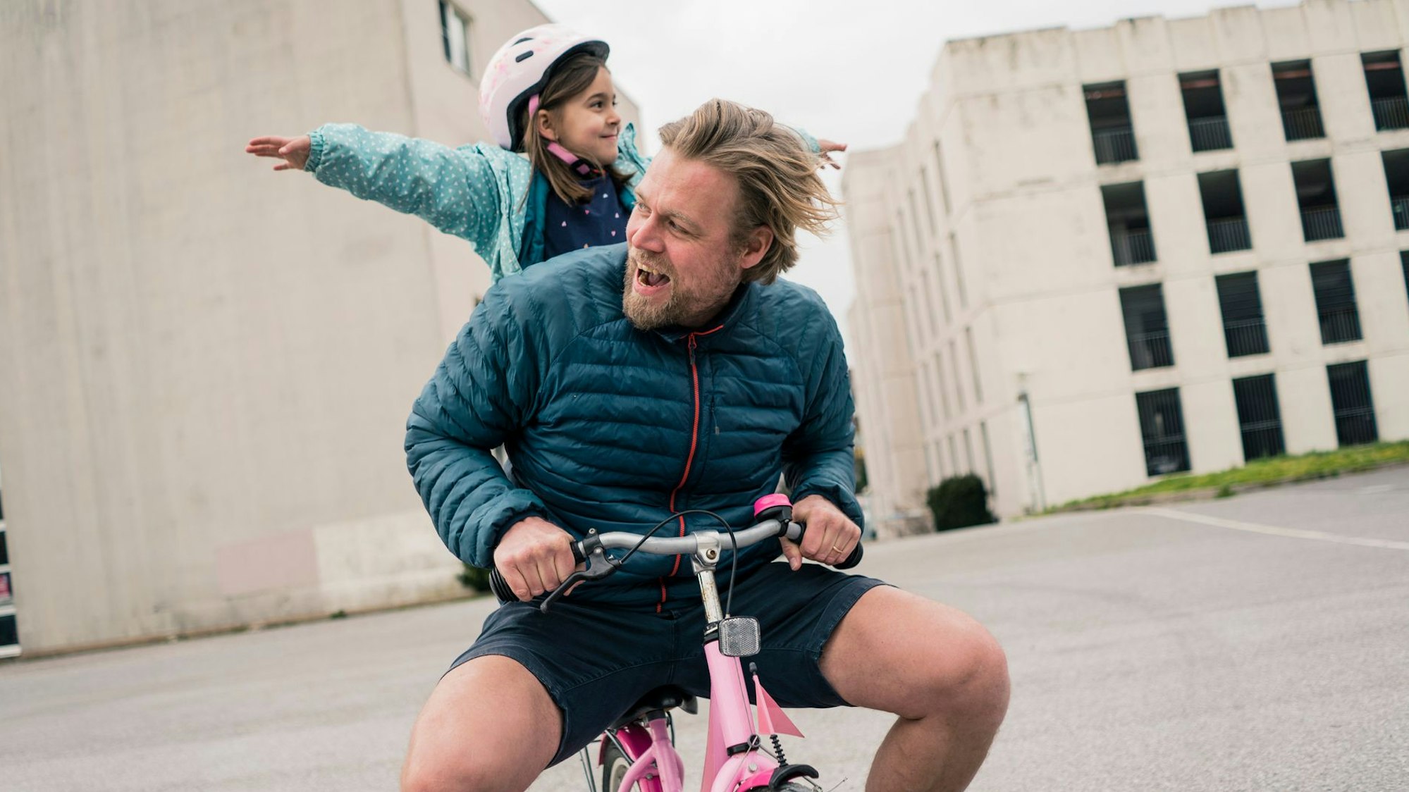 Junger Vater sitzt mit seinem Kind auf einem pinkfarbenen Dreirad (Symbolbild)