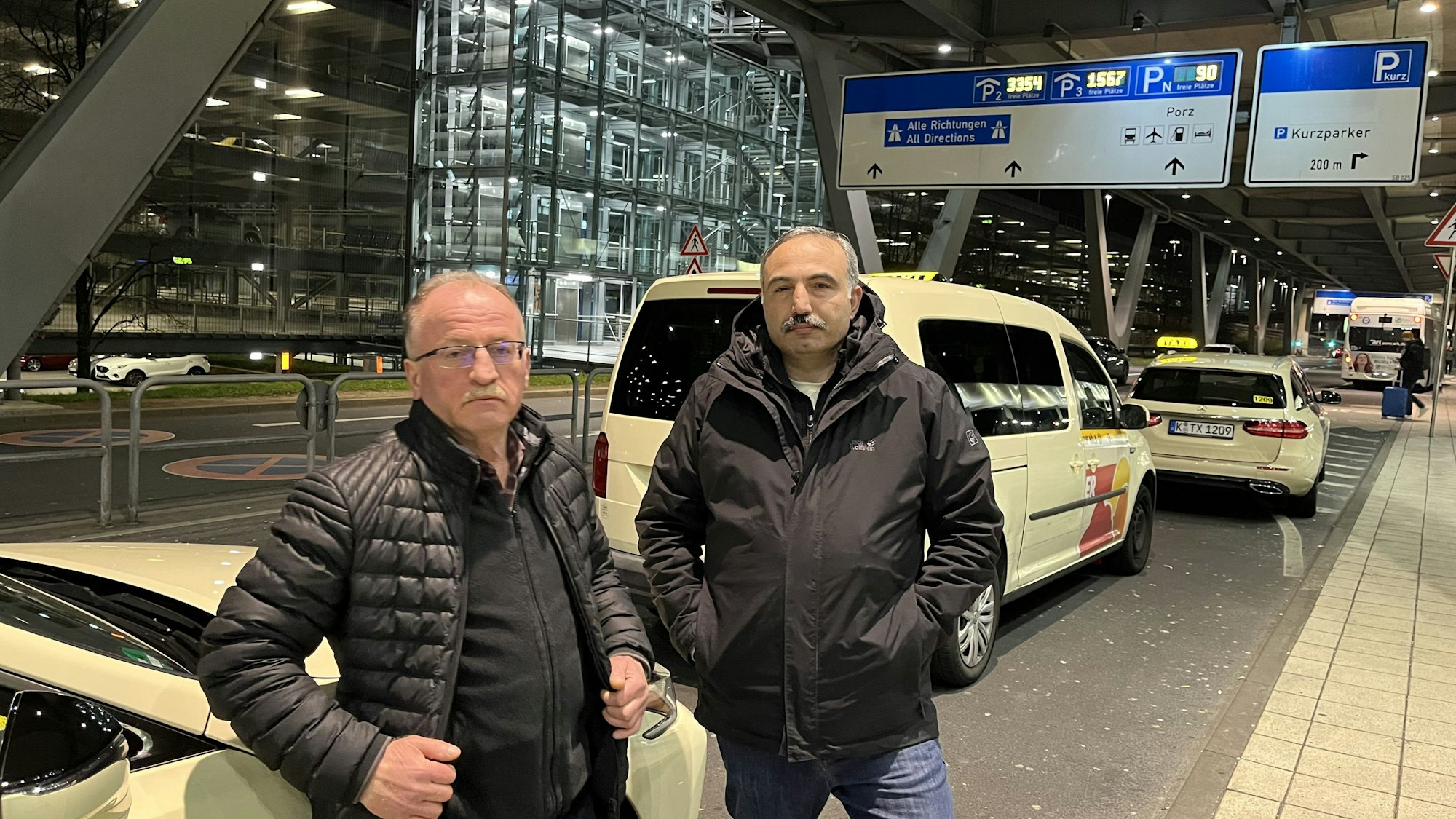 Die Taxifahrer Muzaffer und Imdat stehen vor dem Terminal 2 des Flughafens und warten auf Kunden.