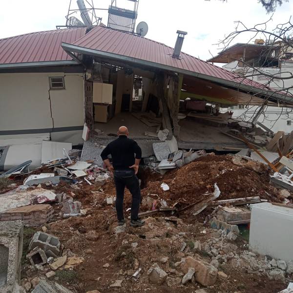 Ein Mann steht vor einem durch das Erdbeben in der Türkei zerstörten Haus.