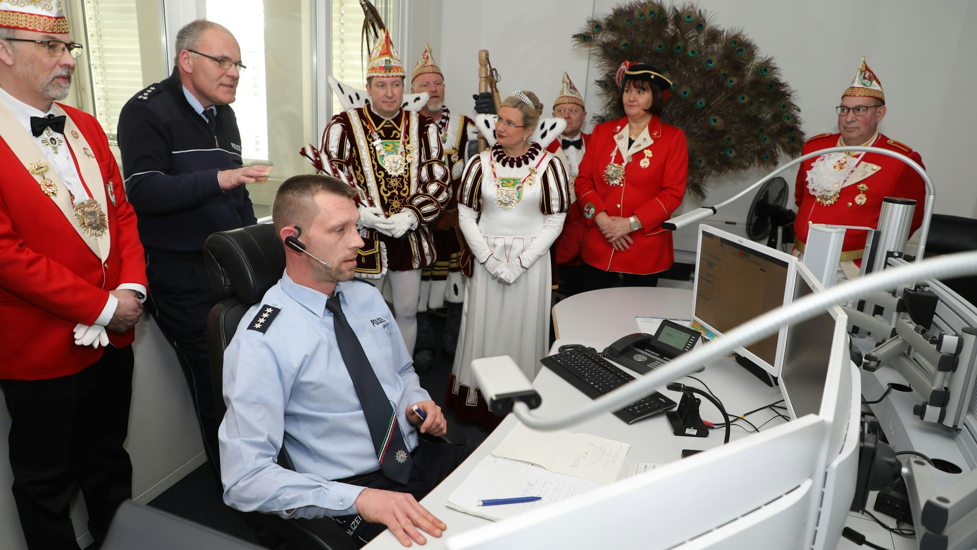 Bergisch Gladbachs Dreigestirn besichtigt mit seinem Gefolge die Leitstelle der Kreispolizei. Ein Polizeibeamter sitzt dort vor Bildschirmen.