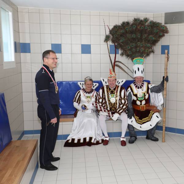 Der Leiter der Polizeiwache Bergisch Gladbach steht in der Sammelzelle des Polizeigewahrsams, das Dreigestirn sitzt auf einer Pritsche.