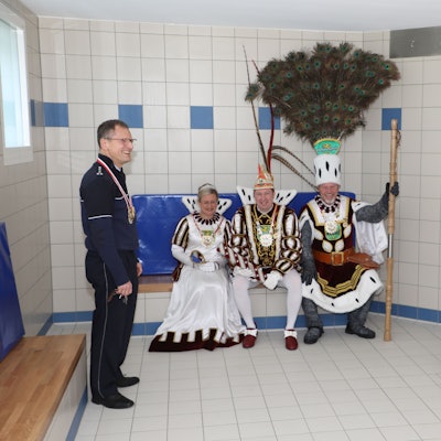 Der Leiter der Polizeiwache Bergisch Gladbach steht in der Sammelzelle des Polizeigewahrsams, das Dreigestirn sitzt auf einer Pritsche.