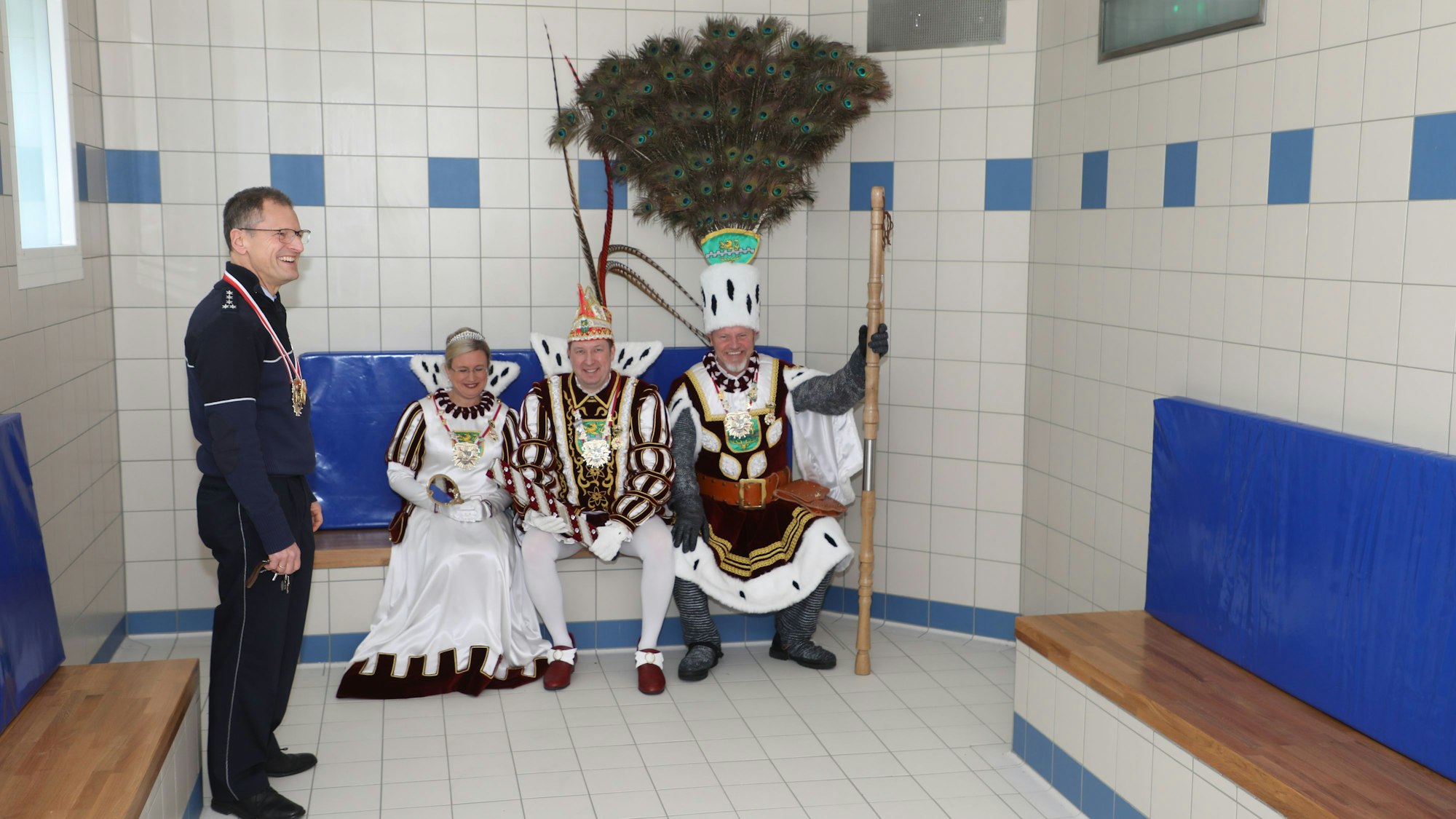 Der Leiter der Polizeiwache Bergisch Gladbach steht in der Sammelzelle des Polizeigewahrsams, das Dreigestirn sitzt auf einer Pritsche.