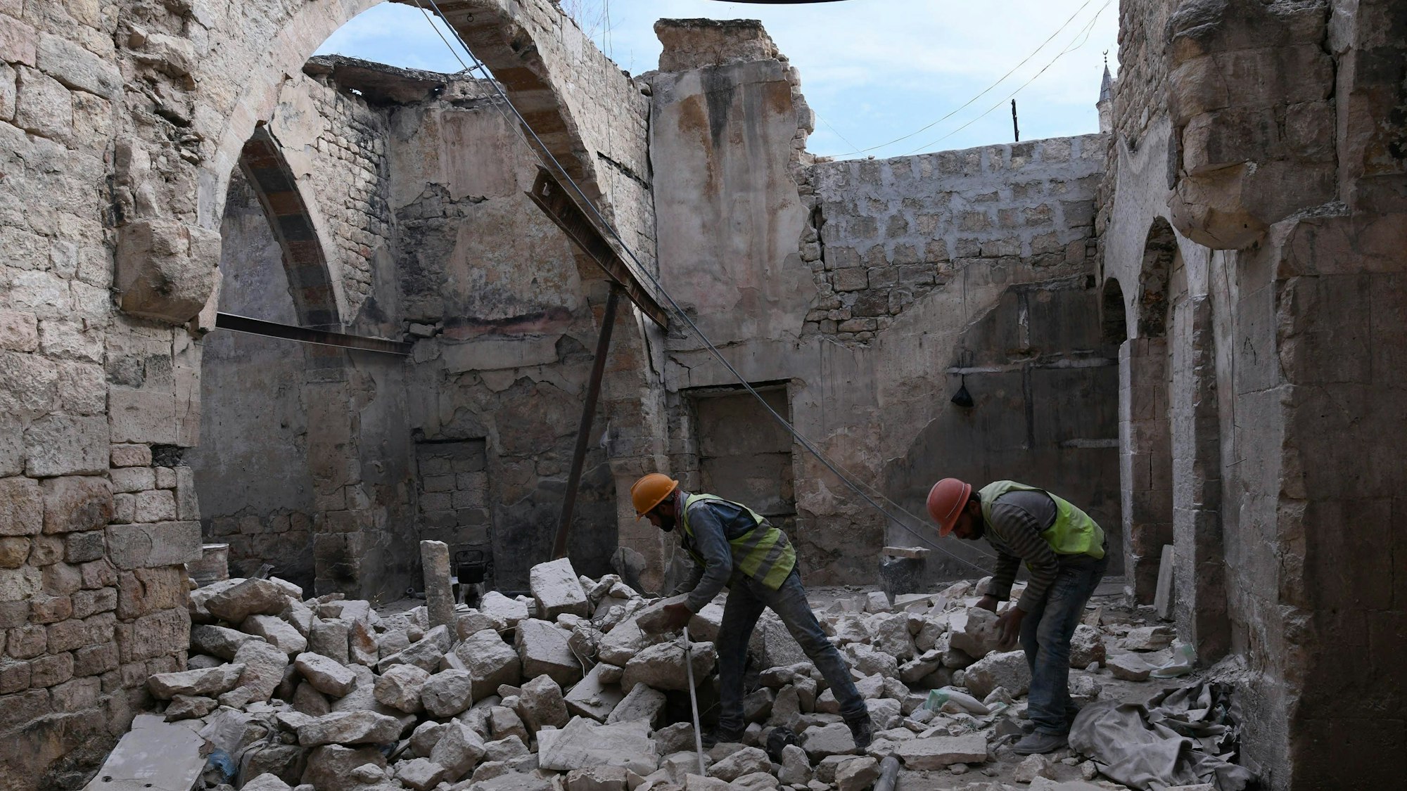Bauarbeiter stehen beim Wiederaufbau des Khabiya Markts im historischen Viertel Souk der Altstadt von Aleppo zwischen Trümmern eines zerstörten Gebäudes. (2019)