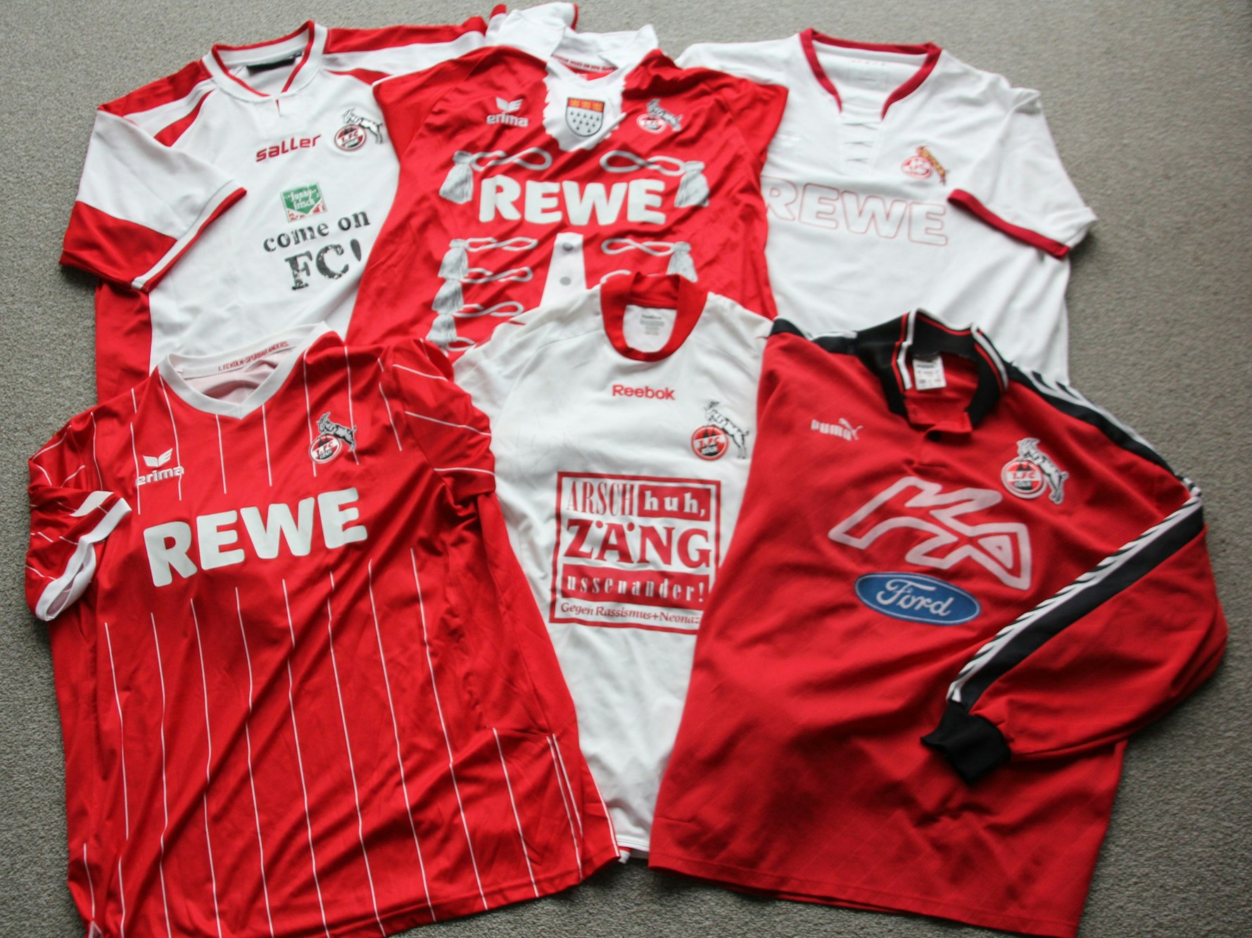 Eine Sammlung von verschiedenen Sondertrikots des 1. FC Köln zu unterschiedlichen Anlässen. Auf dem einen steht etwas Come On, FC. Auf einem anderen ist das Ford-Modell Ka beworben.
