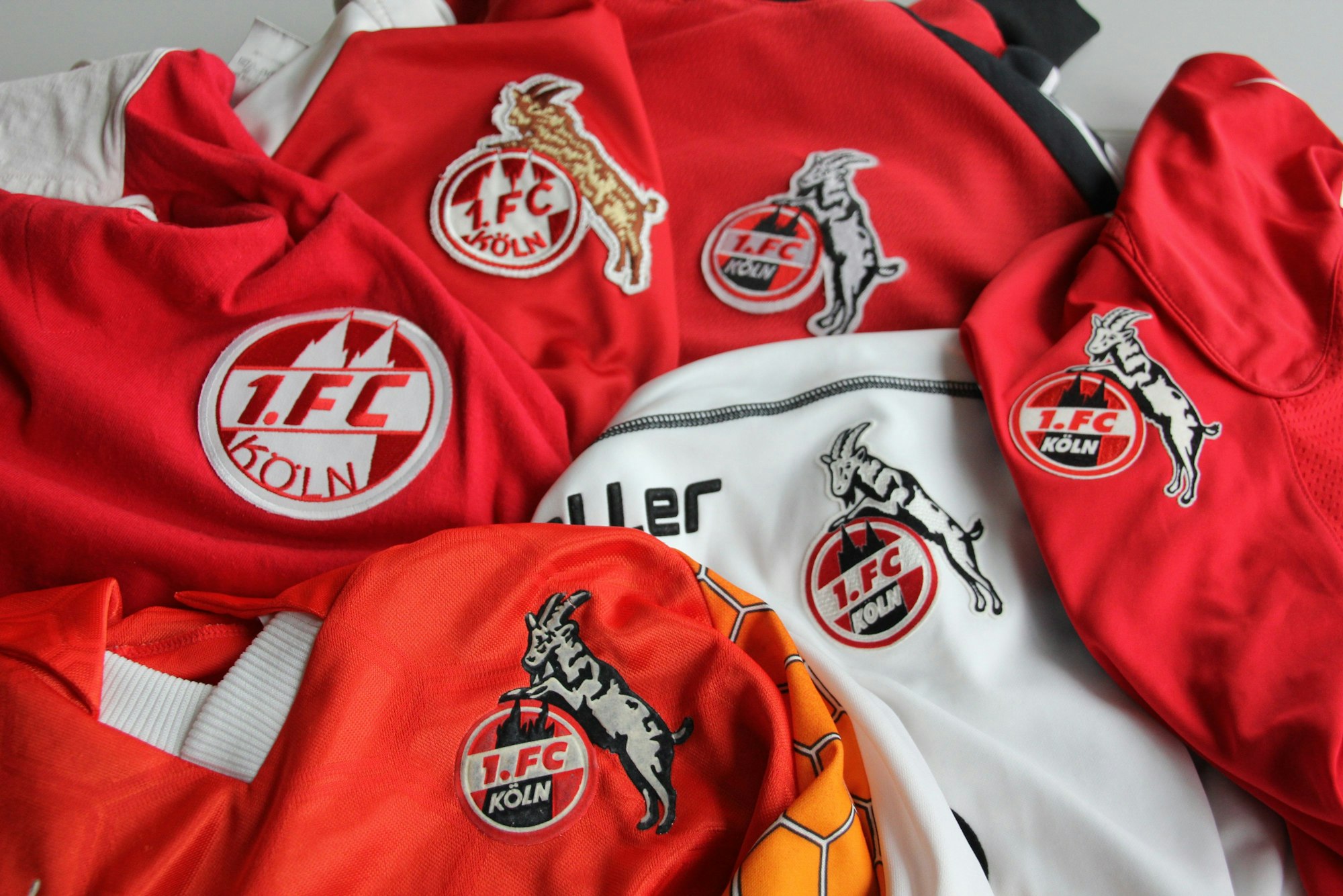 Kreisförmig angeordnet, unterschiedliche Varianten des Logos des 1. FC Köln, mit und ohne Geißbock.