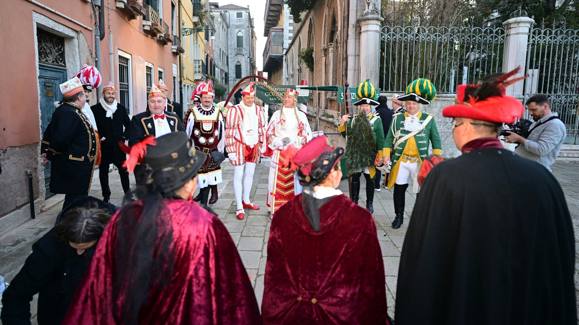 Das Kölner Dreigestirn steht mit mehreren Menschen in einer Gasse in Venedig.
