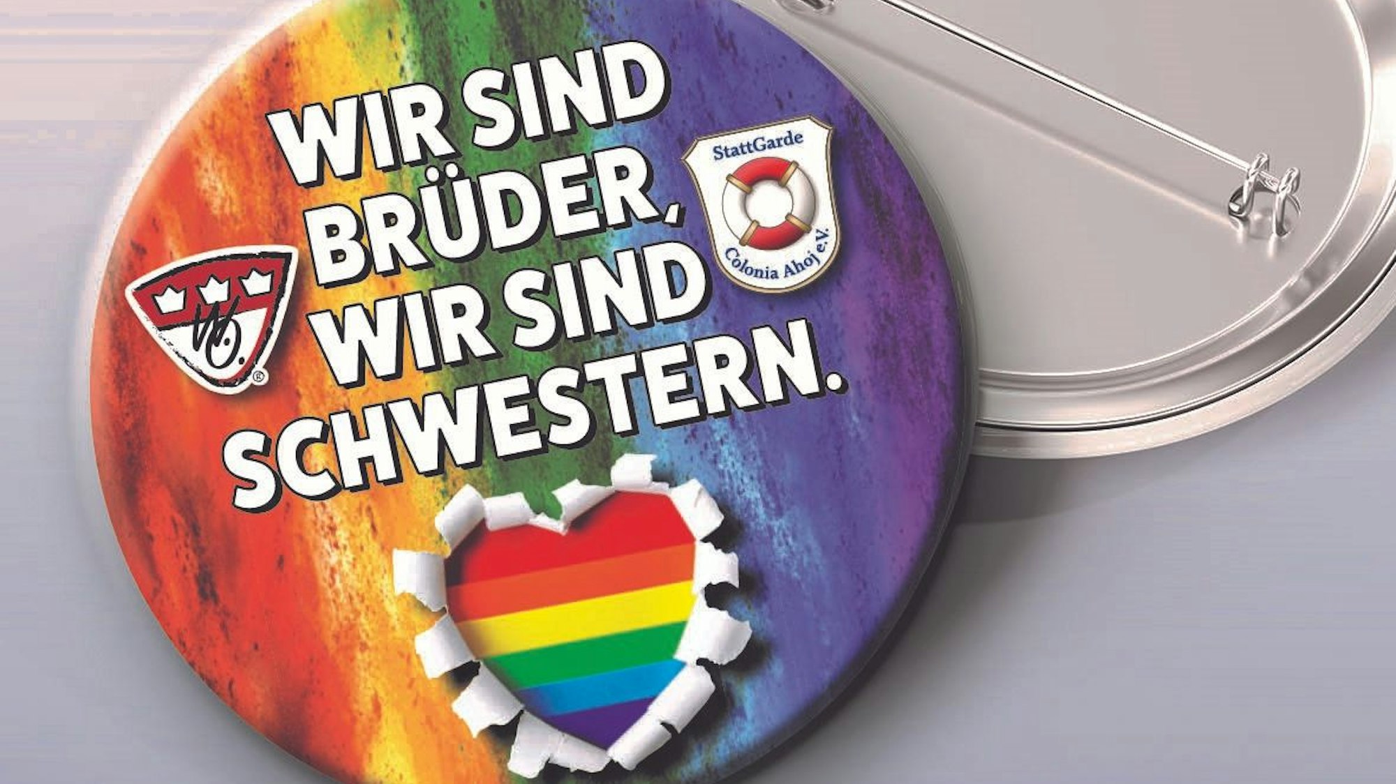 Der Pin ist in Regenbogen-Farben gestaltet, darauf steht ein Zitat aus dem Brings-Song „Liebe gewinnt“: „Wir sind Brüder, wir sind Schwestern“.