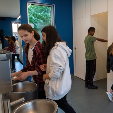 Ein Junge und ein Mädchen gehen durch eine Tür auf die Toilette. Im Vordergrund waschen sich zwei Mädchen die Hände.