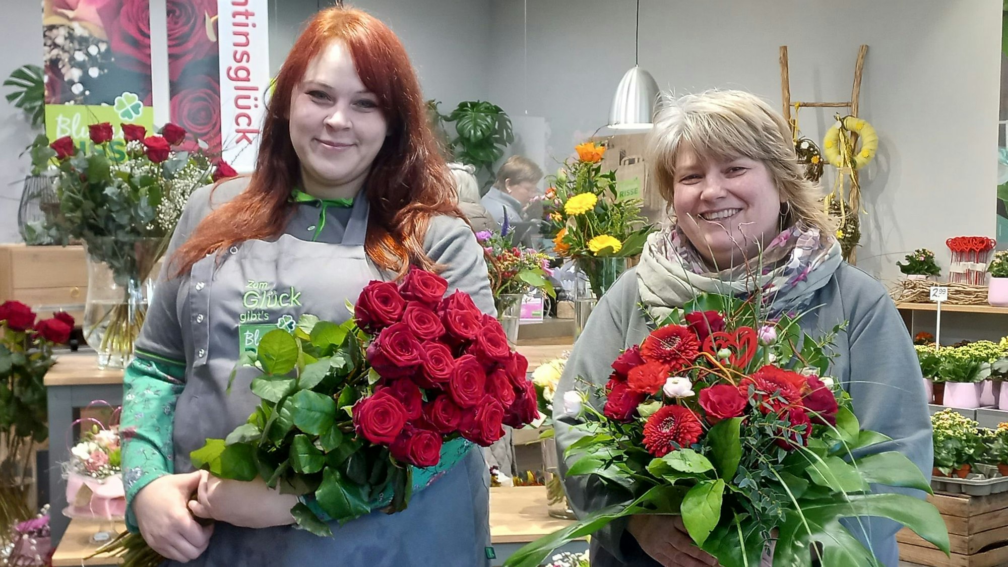 Die Floristinnen Nadine Grenda und Annika Brühl halten zwei dicke Rosensträuße.