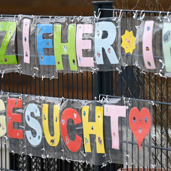 Es sind Schilder mit den Worten „Erzieher*in gesucht“ an einem Zaun beschäftigt.