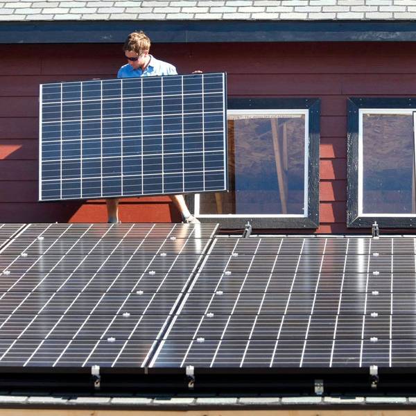 Es sind zwei Arbeiter zu sehen, die auf einem Dach Solarpaneelen befestigen.