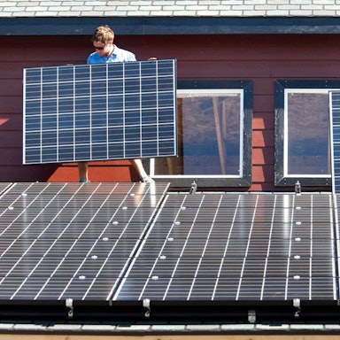 Es sind zwei Arbeiter zu sehen, die auf einem Dach Solarpaneelen befestigen.