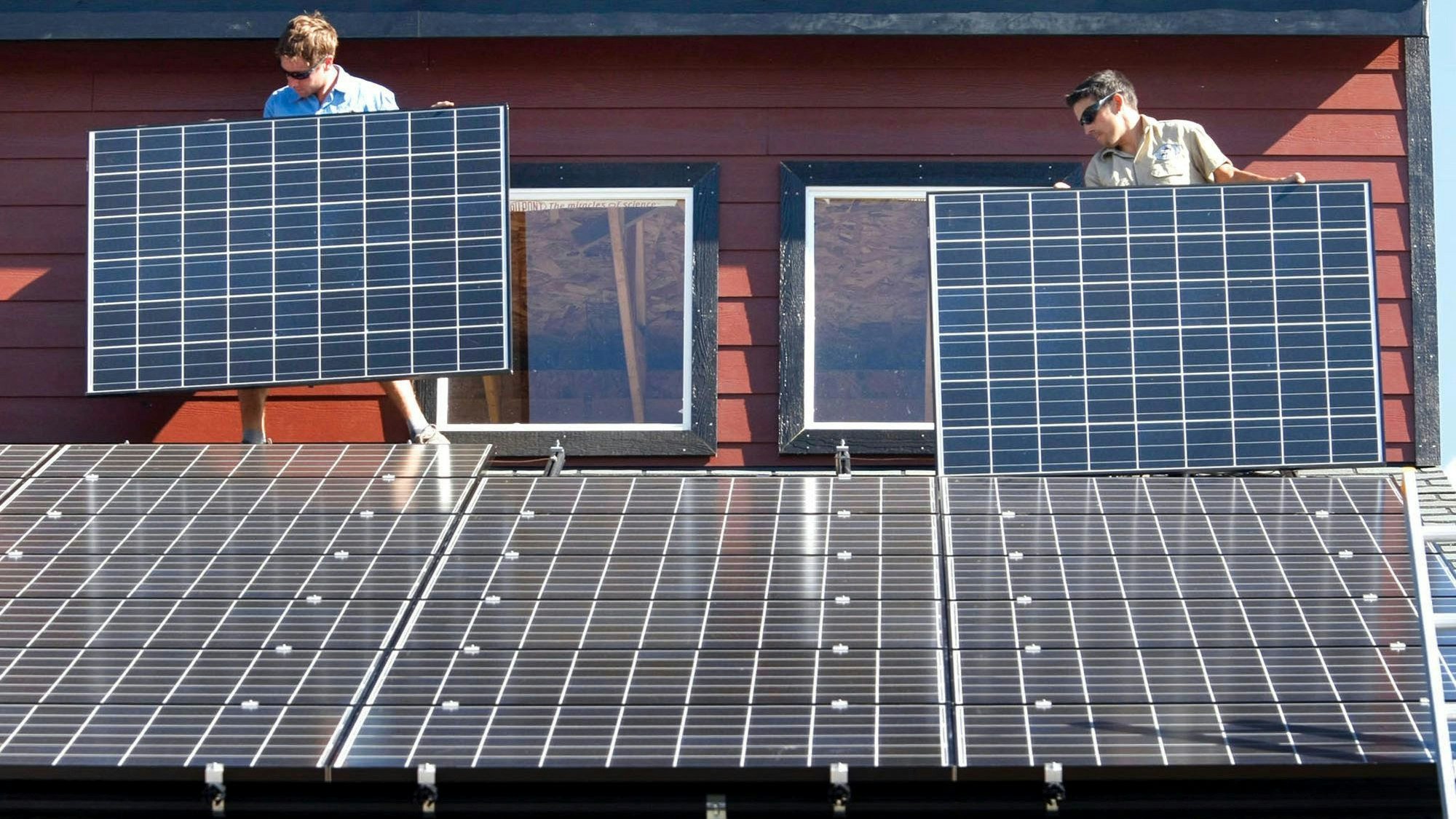 Es sind zwei Arbeiter zu sehen, die auf einem Dach Solarpaneelen befestigen.