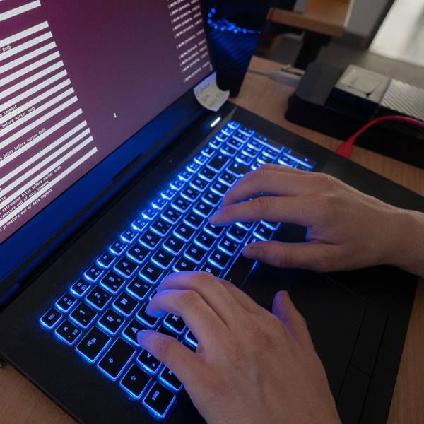 Zwei Hände tippen an einem Laptop mit leuchtender Tastatur.