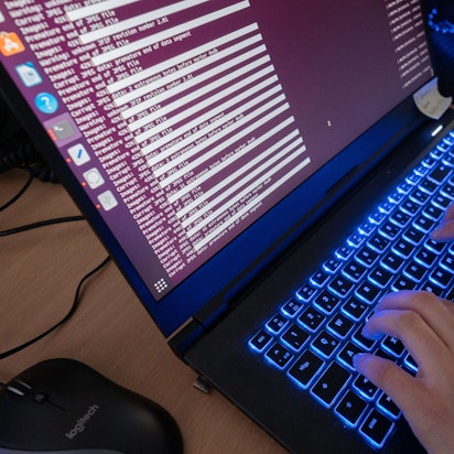 Zwei Hände tippen an einem Laptop mit leuchtender Tastatur.