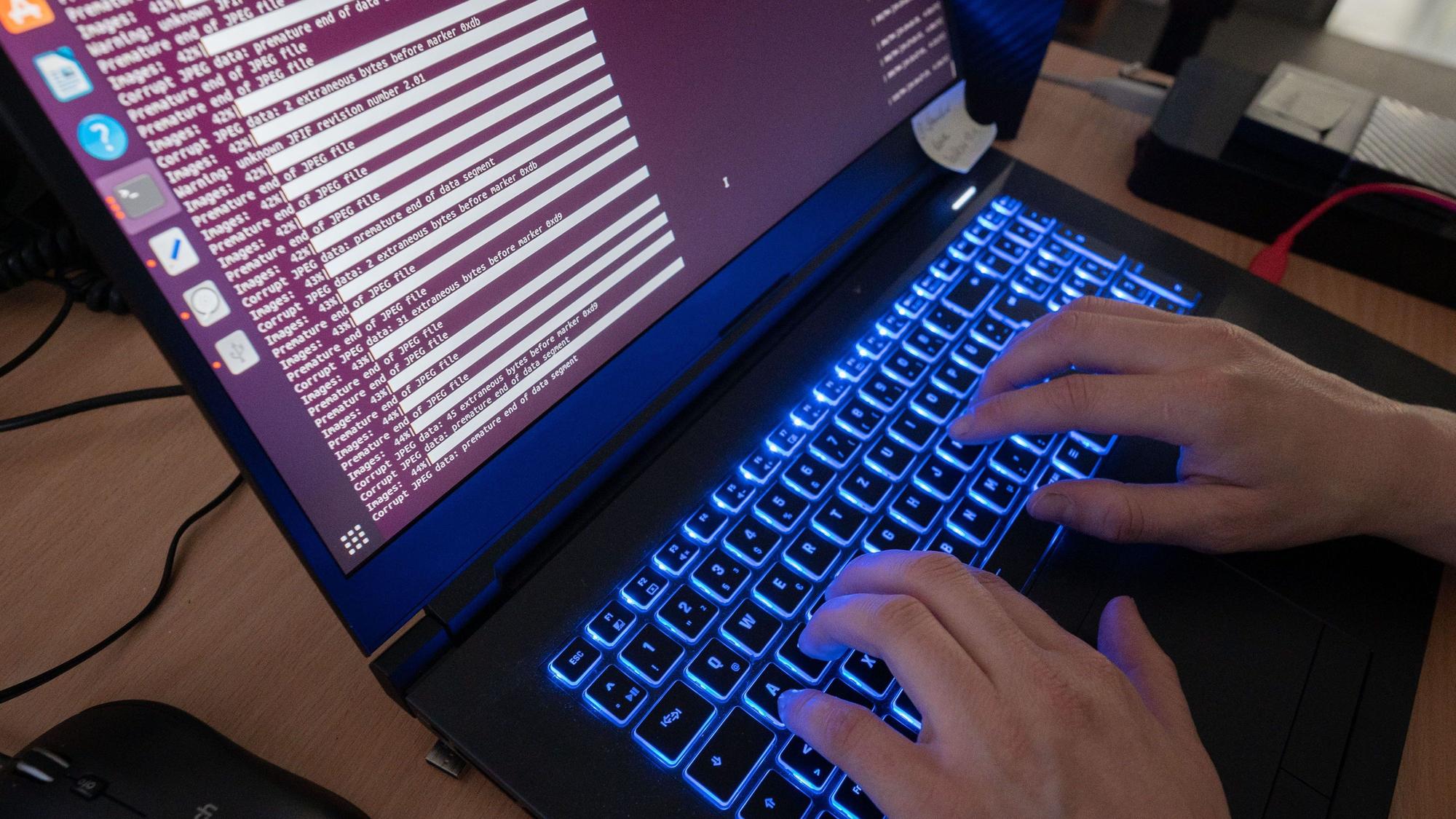 Zwei Hände tippen an einem Laptop mit leuchtender Tastatur.