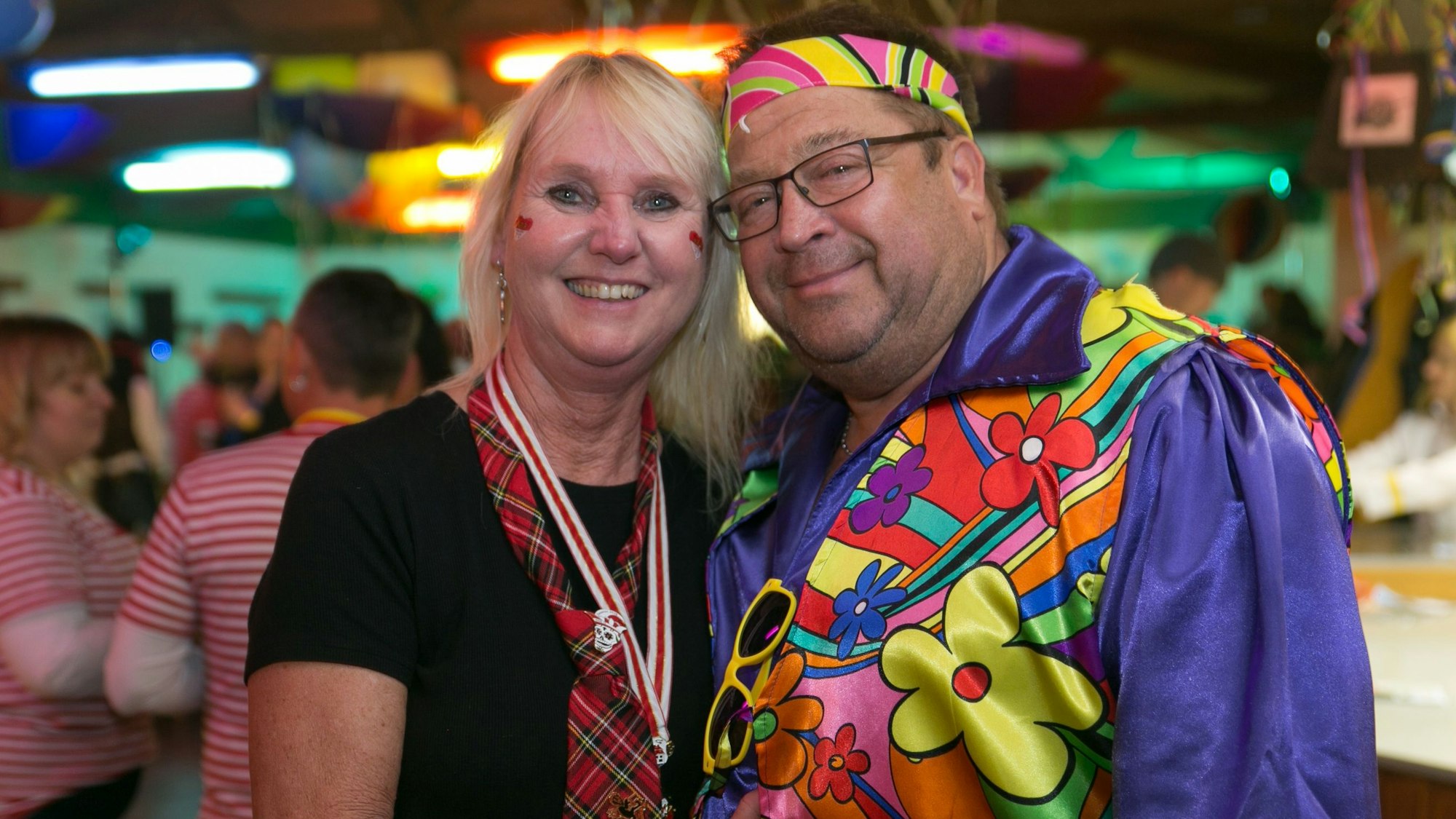 Ein als Schottin und Hippie kostümiertes Pärchen lächelt gemeinsam in die Kamera.