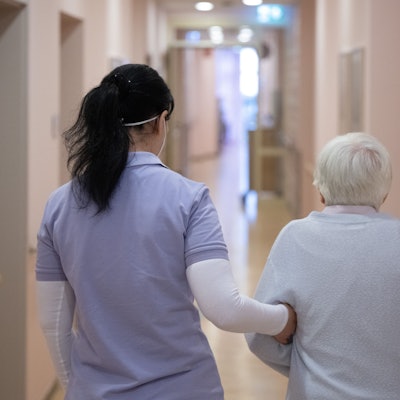 Eine Pflegefachkraft geht mit einer alten Frau über den Gang eines Pflegeheims.