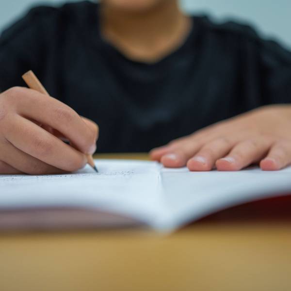 Ein Grundschüler sitzt an einem Tisch und schreibt mit einem Bleistift in sein Heft.