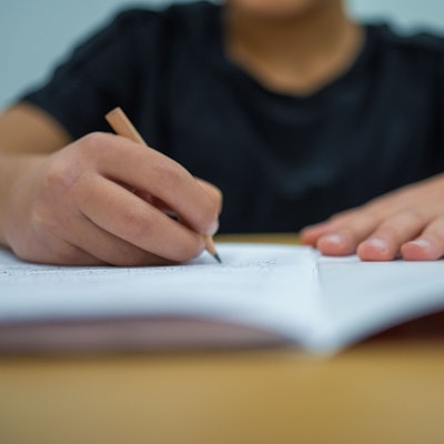 Ein Grundschüler sitzt an einem Tisch und schreibt mit einem Bleistift in sein Heft.