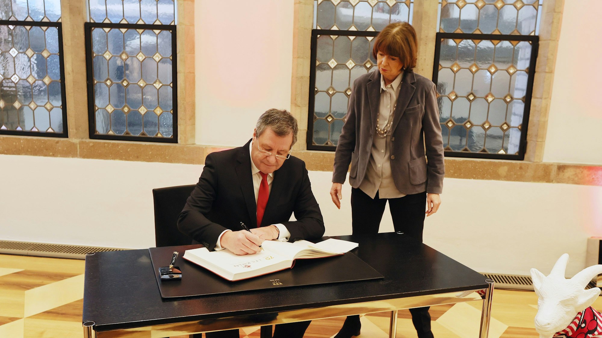 Werner Wolf schreibt ins Gästebuch der Stadt Köln und Henriette Reker steht hinter ihm.