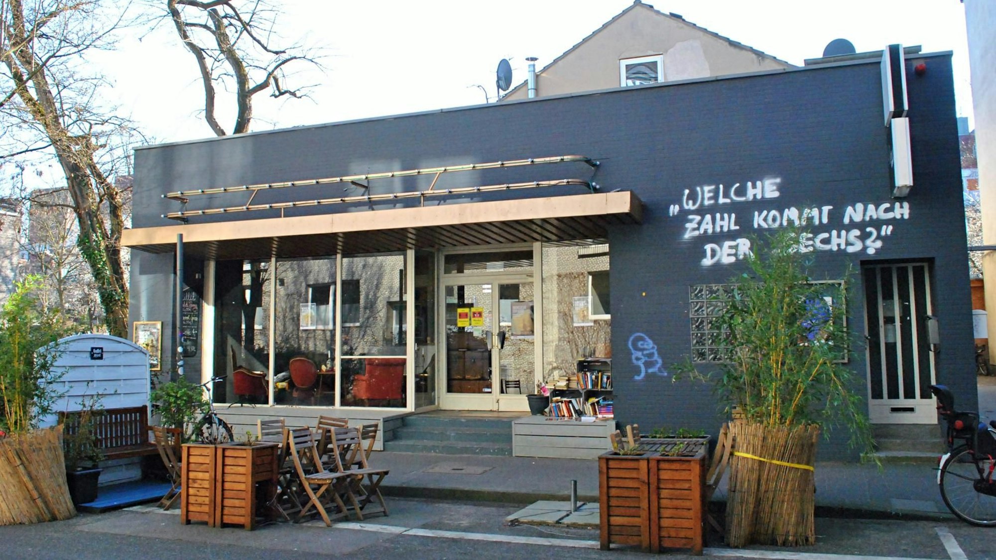 Das Urania Theater in Köln-Ehrenfeld von außen fotografiert, ein kleiner Gebäudekomplex mit einzelnen Tischen