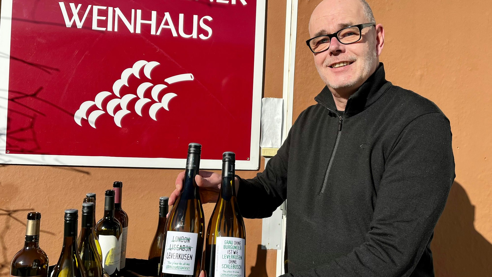 Klaus Klein vor dem Leverkusener Weinhaus mit zwei Flaschen Wein