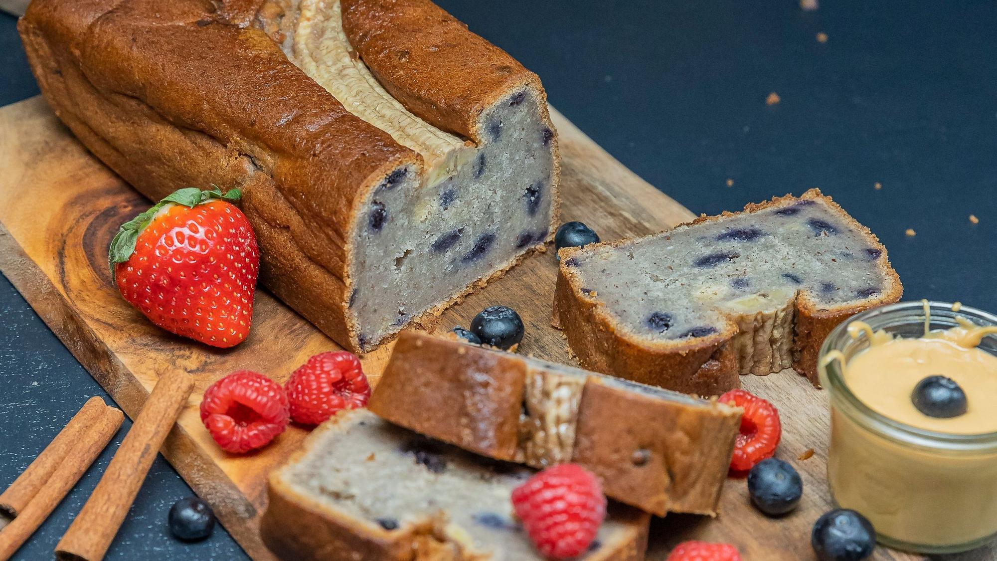 Das Bananenbrot liegt auf einem Holzbrettchen, zusammen mit Heidel- und Himbeeren