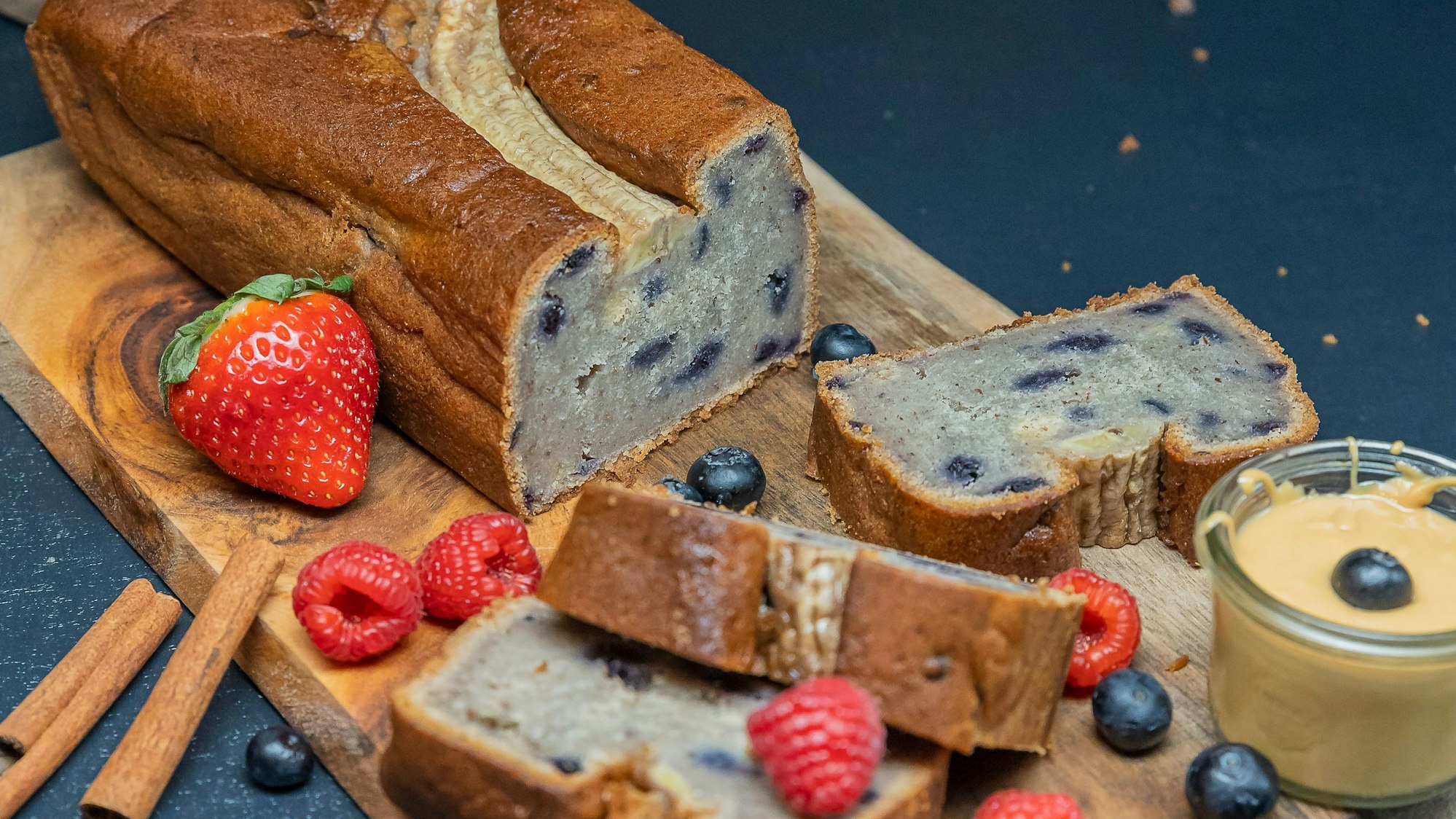Das Bananenbrot liegt auf einem Holzbrettchen, zusammen mit Heidel- und Himbeeren