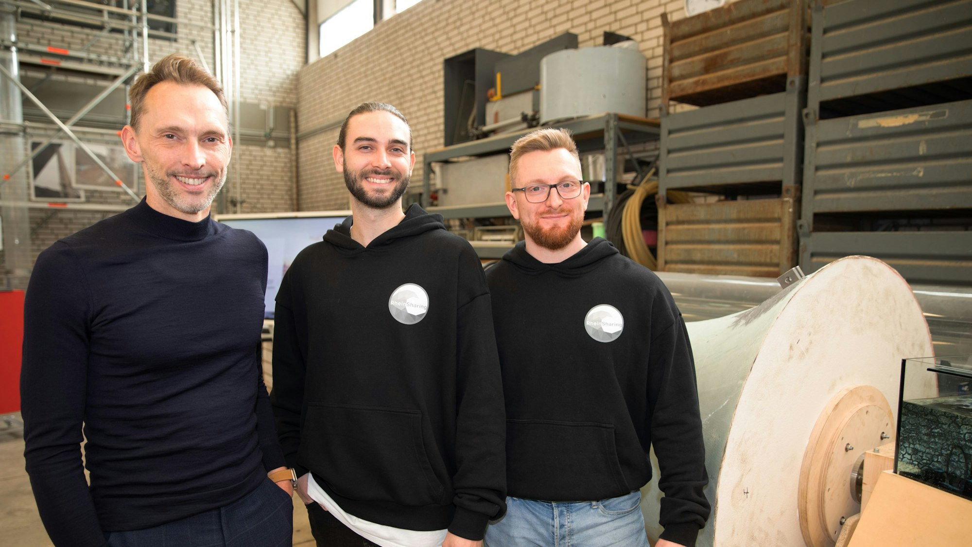 Köln-Business-Geschäftsführer Manfred Janssen mit Felix Roder und Marcel Heilich von „Rheinsharing“ stehen vor dem Prototyp des Kraftwerks. Sie lächeln in die Kamera.