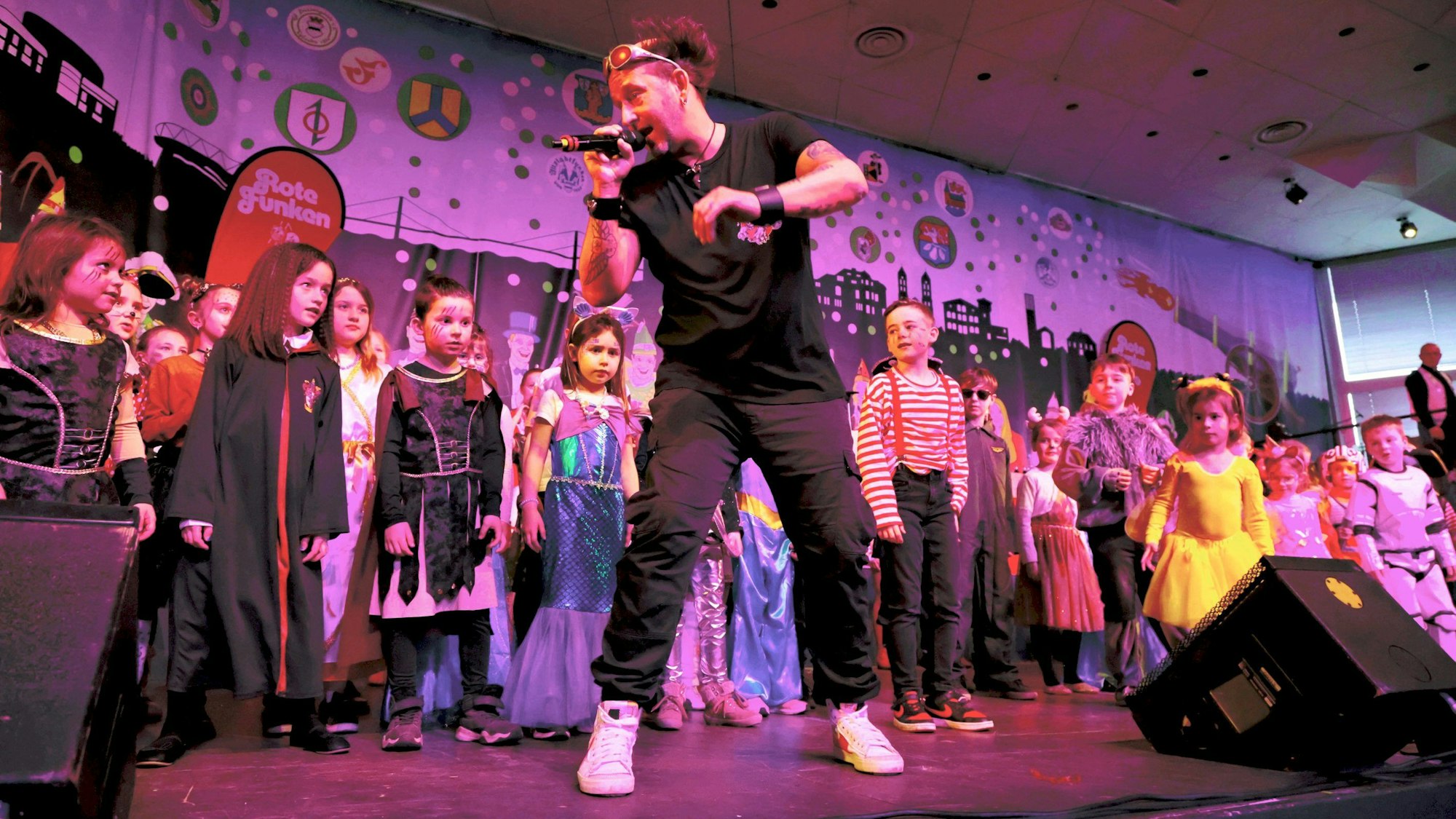 Tom Lehel steht in der Mitte der Bühne, spricht in ein Mikrofon und gibt den mehreren Dutzend Kindern hinter ihm Tanzanweisungen.