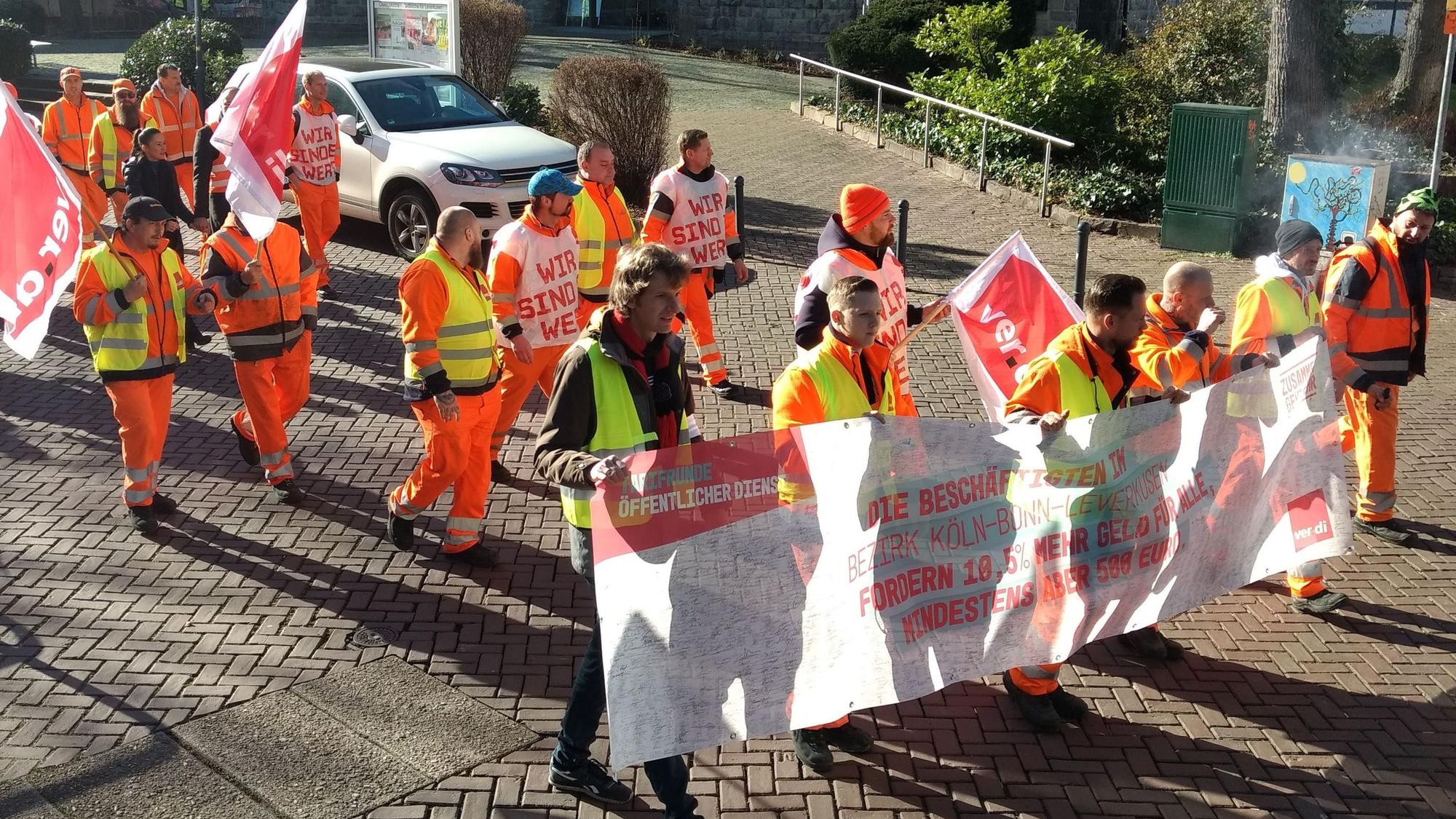 Männer mit Streiktransparenten und Fahnen ziehen durch Wiesdorf.