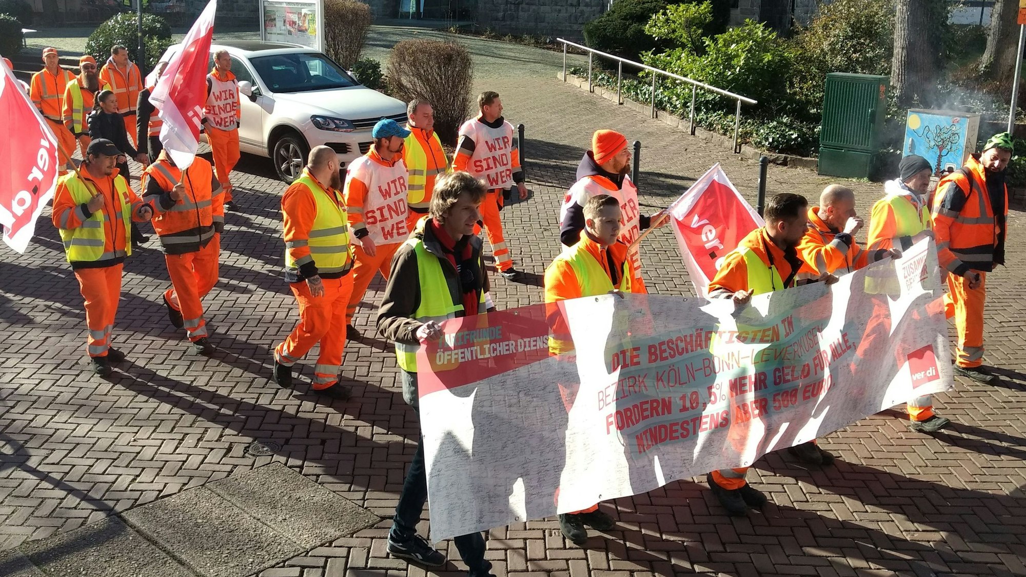 Männer mit Streiktransparenten und Fahnen ziehen durch Wiesdorf.
