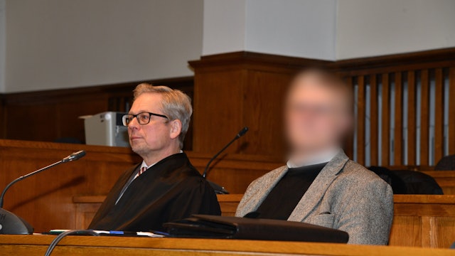 Ein Pfarrer (Gesicht gepixelt) sitzt neben seinem Anwalt im Gerichtssaal.