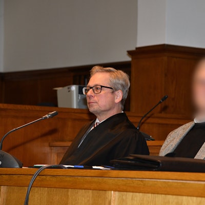 Ein Pfarrer (Gesicht gepixelt) sitzt neben seinem Anwalt im Gerichtssaal.