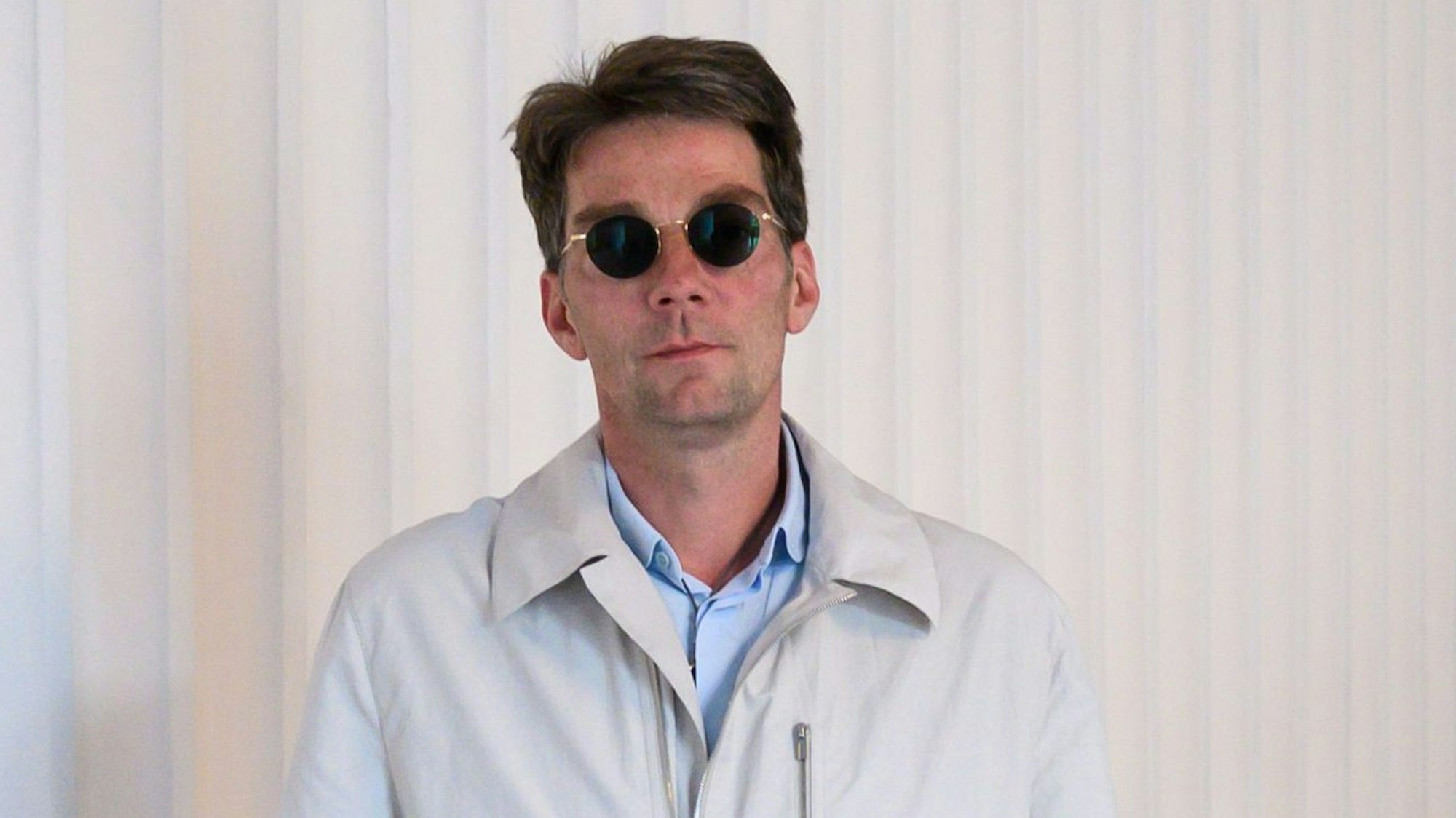 Marco Goecke, Ballettdirektor der Staatsoper Hannover, steht im Foyer der Staatsoper. Er trägt einen hellen Trenchcoat und eine Sonnenbrille.