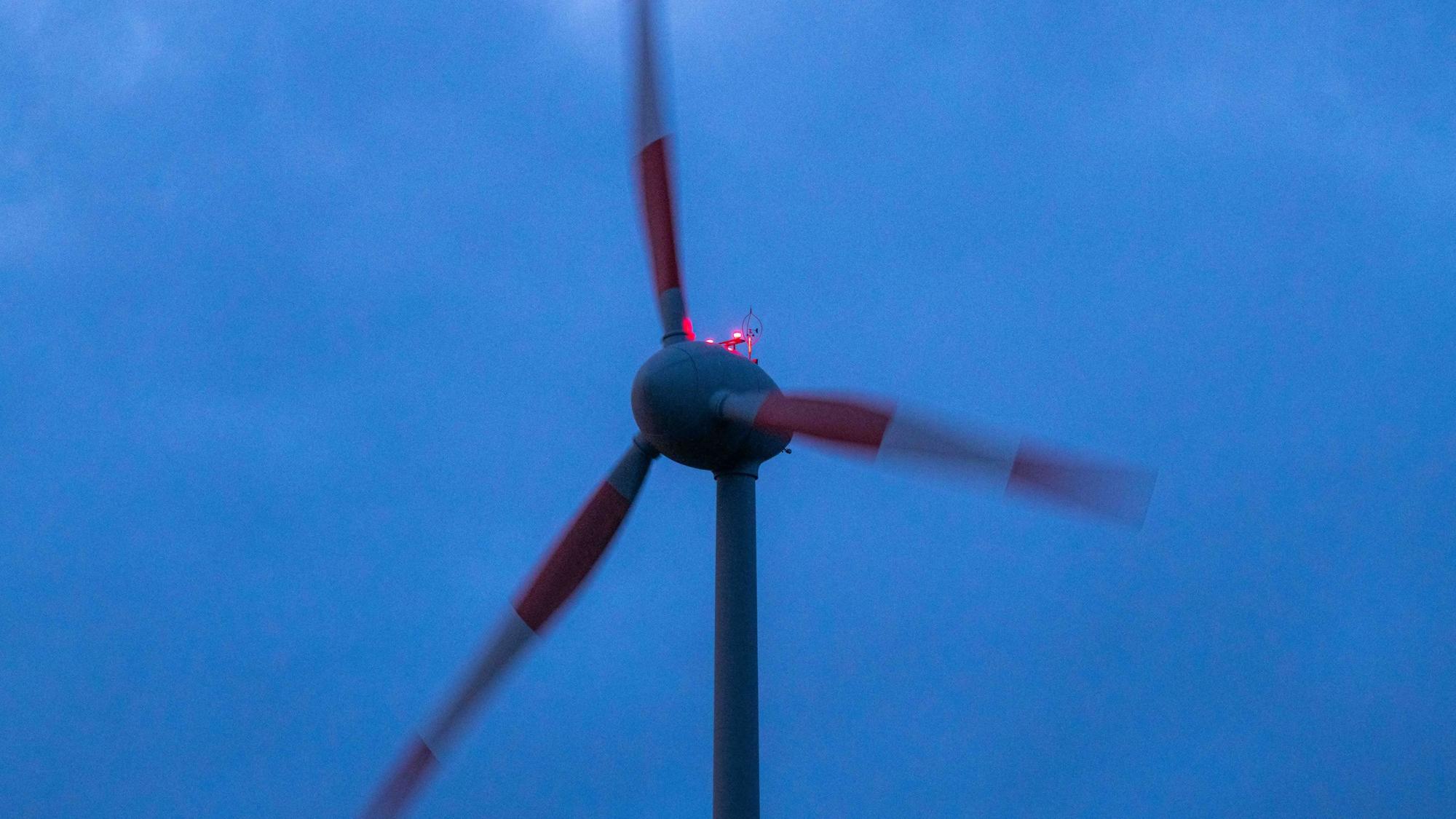 Ein Windrad mit rot-weiß gestreiften Blättern dreht sich vor einem dunklen Himmel.