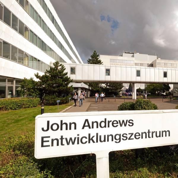 Abgebildet ist ein großes, U-förmiges Gebäude. Im Vordergrund steht ein Schild mit der Aufschrift „John Andrews Entwicklungszentrum“ mit dem blauen, ovalen Ford-Logo.