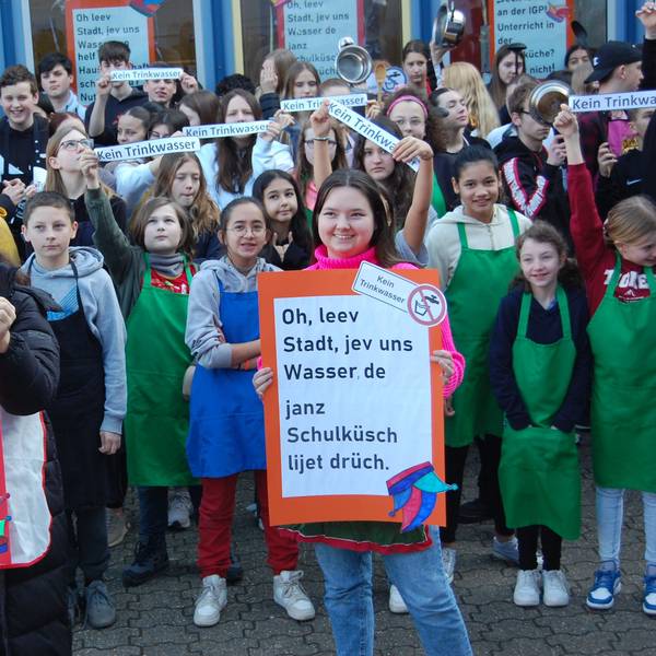 Schüler stehen vor der Schule und halten Protestschilder hoch.